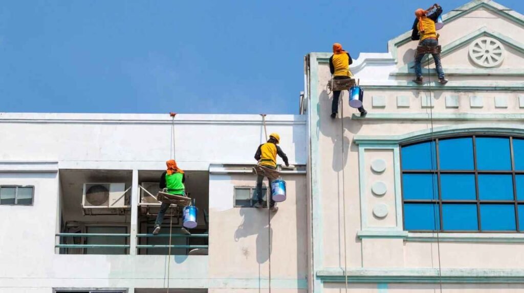 FixitNow team preparing and painting a villa exterior—washing walls, priming, applying reflective coating, modern tools and safety gear.